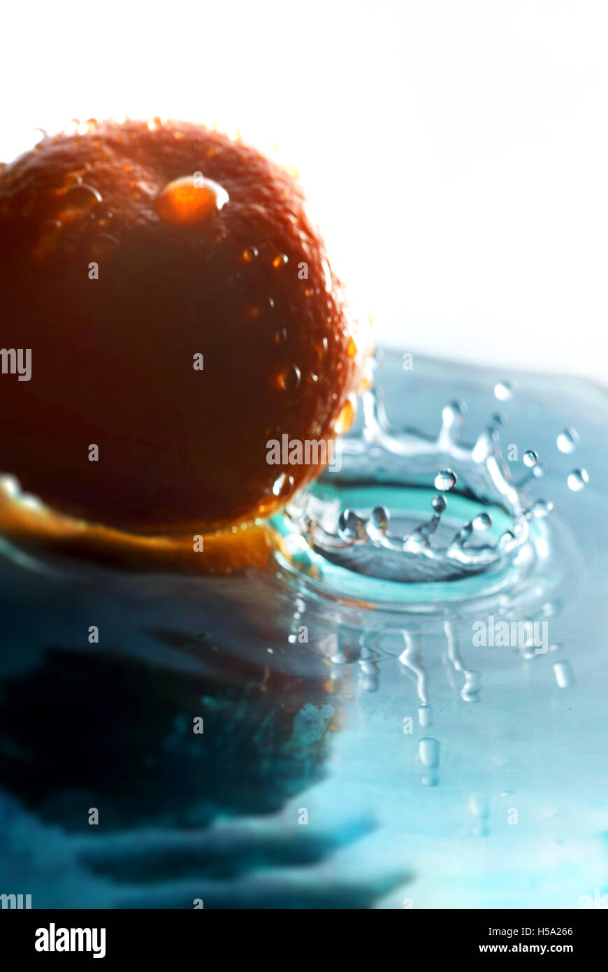 Drip of liquid Making a crown shaped splash next to an orange Stock Photo
