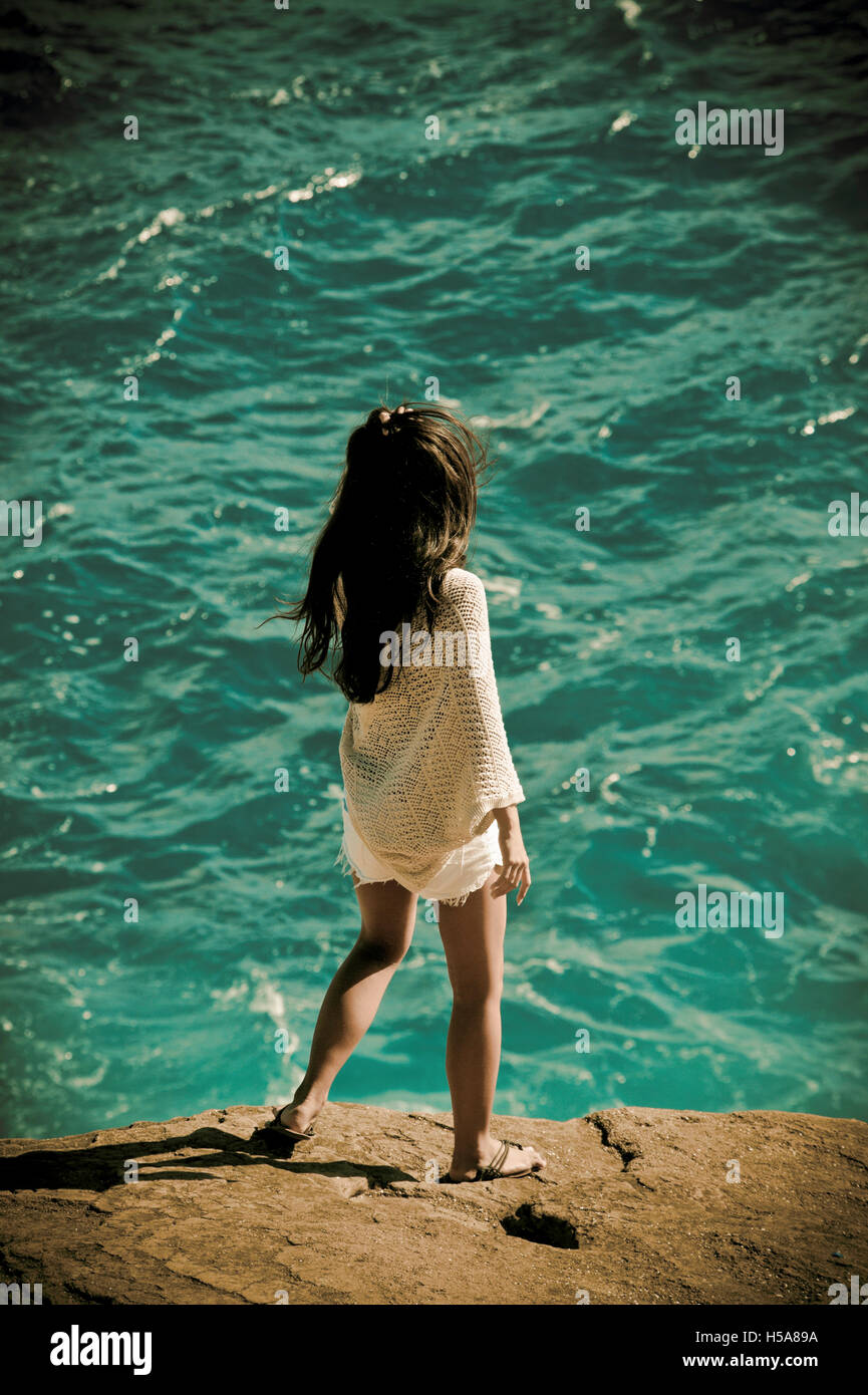 Young woman standing on the edge of a rock by the ocean near Honolulu, Hawaii Stock Photo