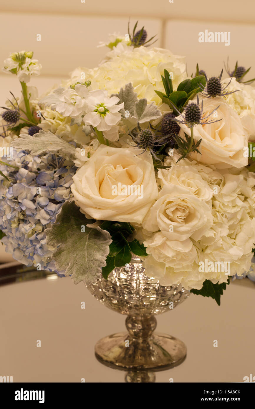 Wedding bouquet in a silver vase on a mirror table with white chairs and a  sofa in the background. Flowers include white poppy P Stock Photo - Alamy
