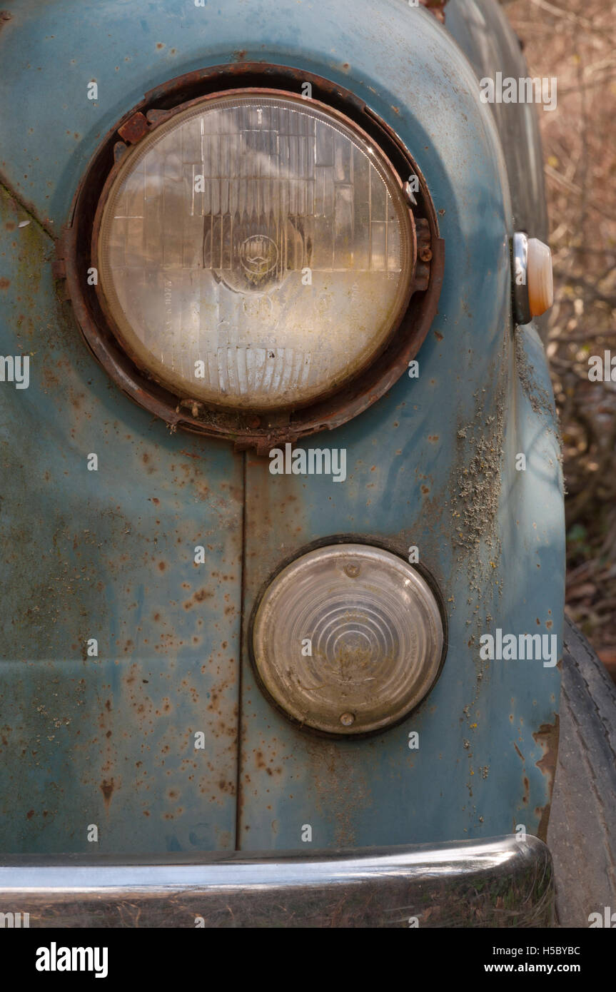 the lights of an old abandoned and rusted car in the weeds Stock Photo