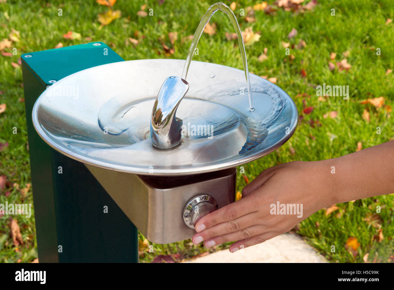 Hand pressing park fountain button, causing water to flow for a cool drink Stock Photo
