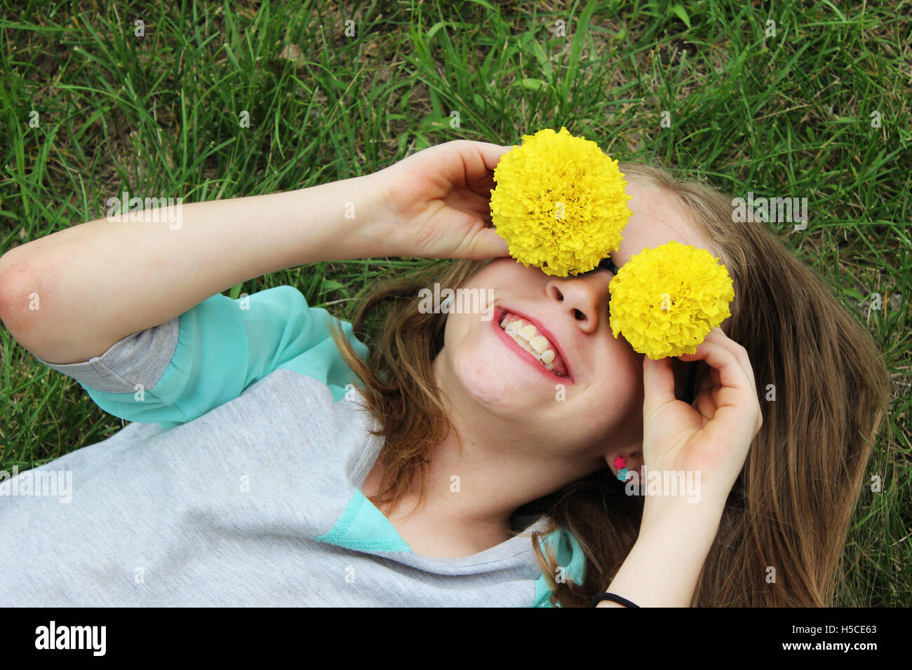 young girl laying in green grass playing with flowers over her eyes and smiling Stock Photo