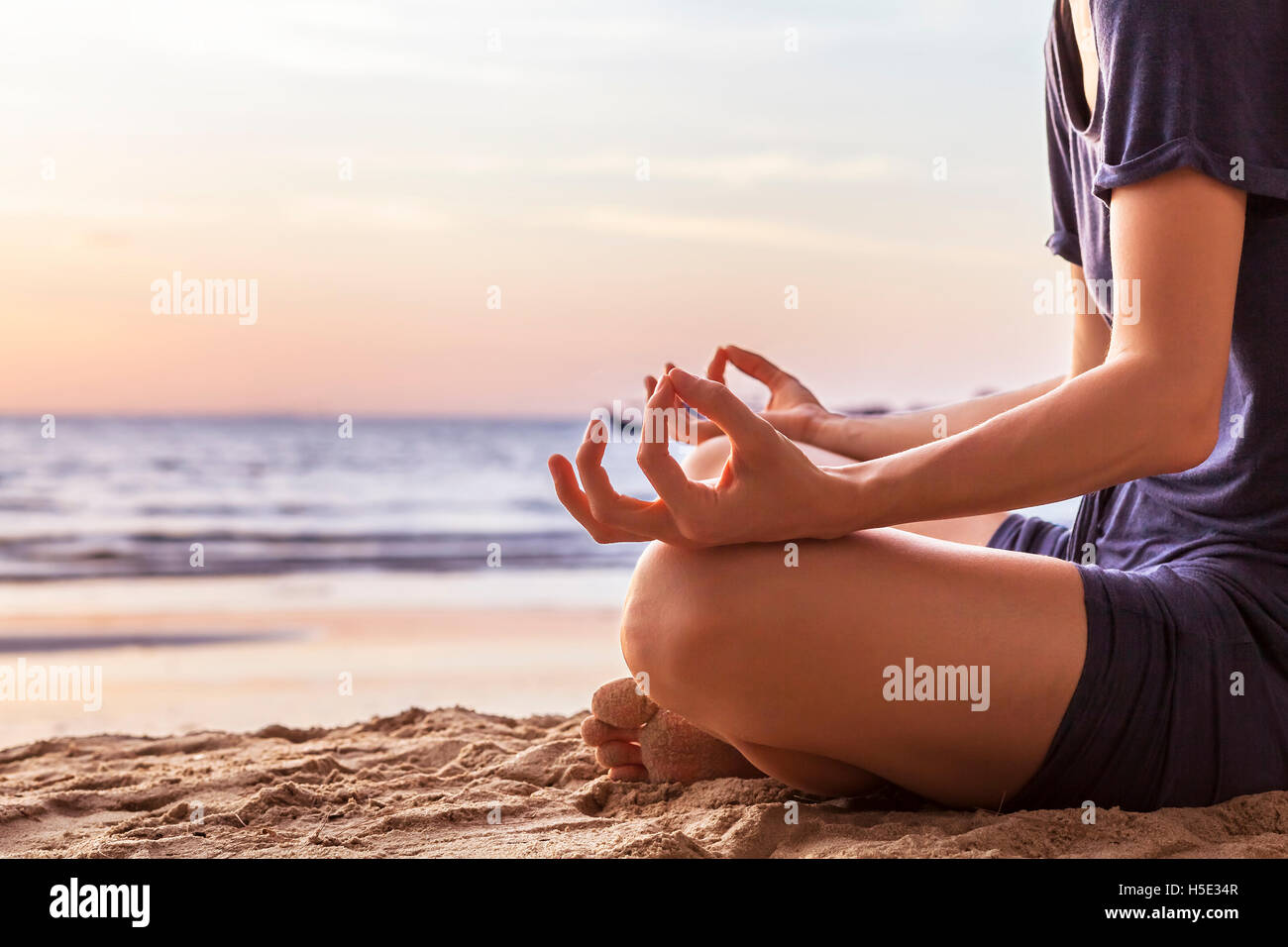 Young woman relaxing by practicing yoga on the beach at sunset, close-up of hands, gyan mudra and lotus position Stock Photo