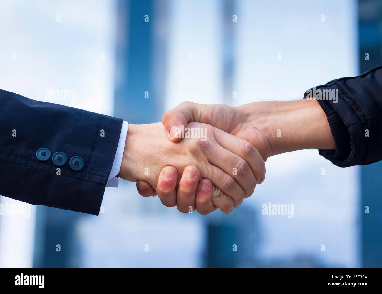 Two businessmen shaking hand with office buildings in background Stock Photo