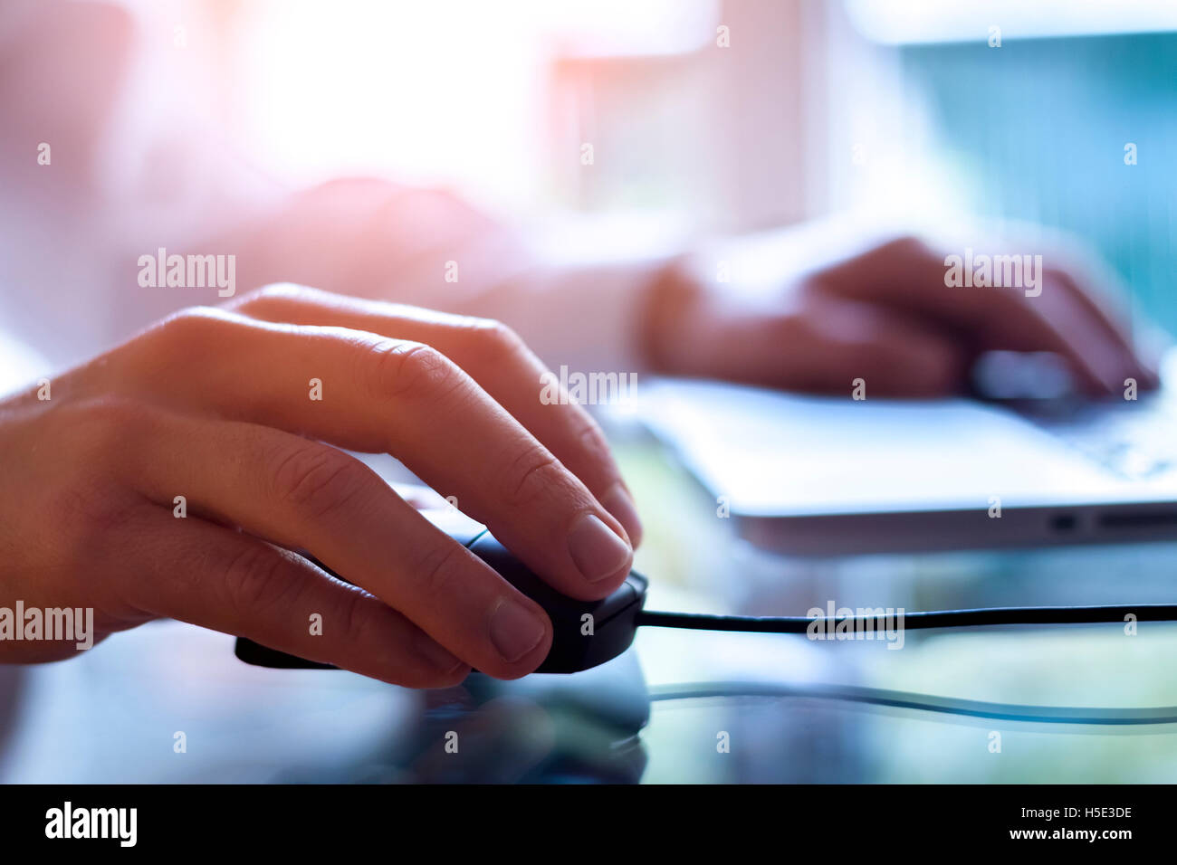 Male hand holding computer mouse with laptop keyboard in the background Stock Photo