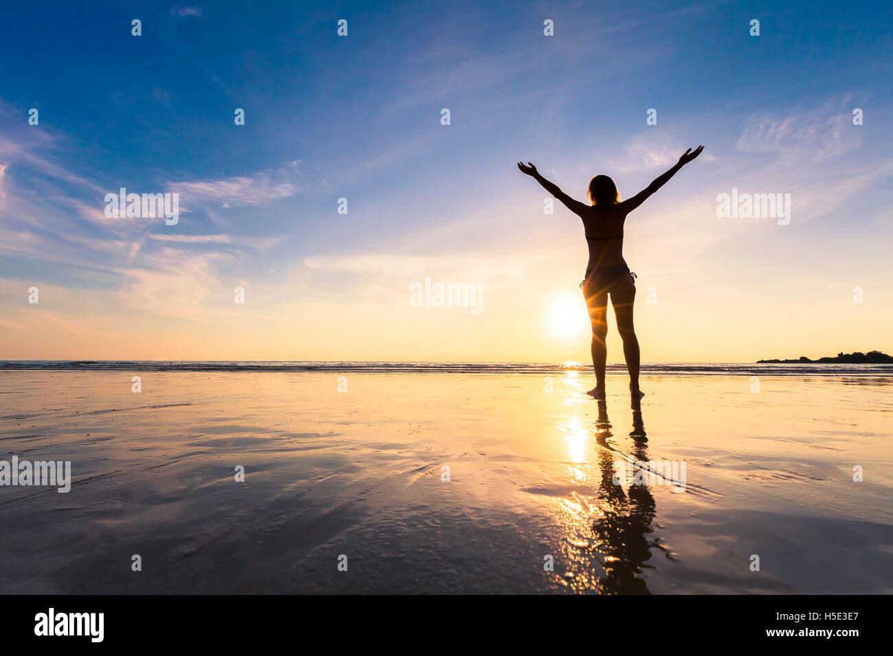 Young happy woman raising hand and revitalizing on a beautiful beach at sunset Stock Photo