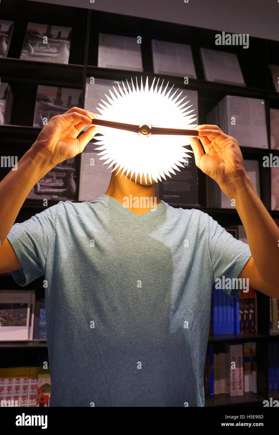 Teenage boy holding a Lumio Book Lamp against his face, creating the illusion of a 'bright idea', Museum of Modern Arts, NYC USA Stock Photo