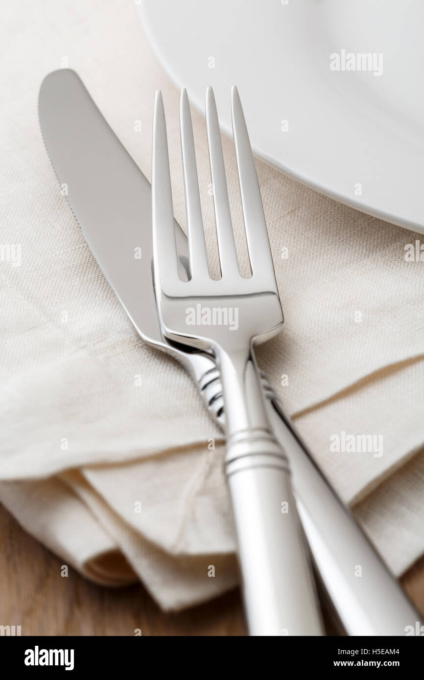 Simple, classic table setting place setting with high quality silverware fork and knife on cloth napkin and white china plate. Stock Photo