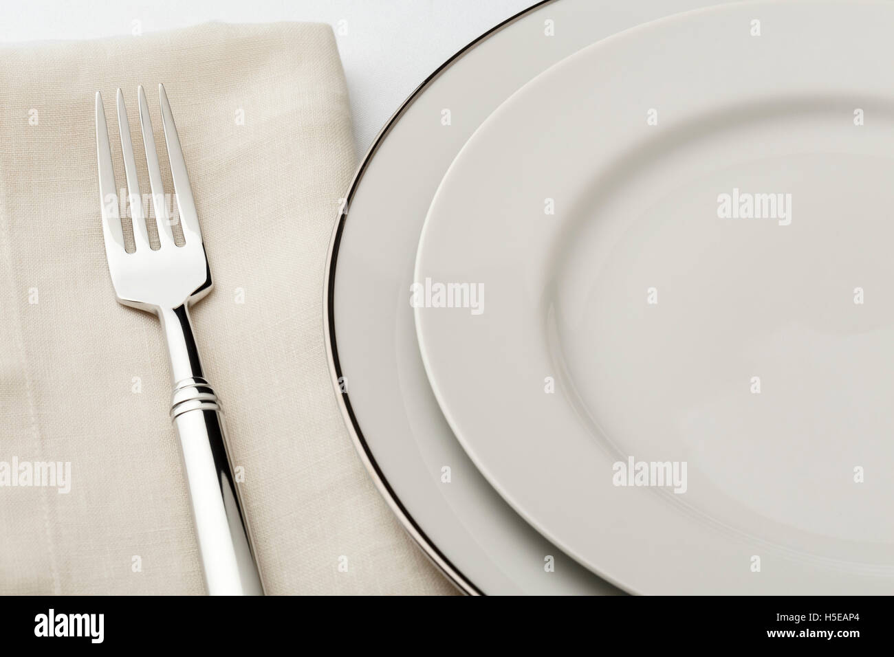 Fine dining table setting place setting with high quality classic style white china dishes, linen napkin and silverware fork Stock Photo