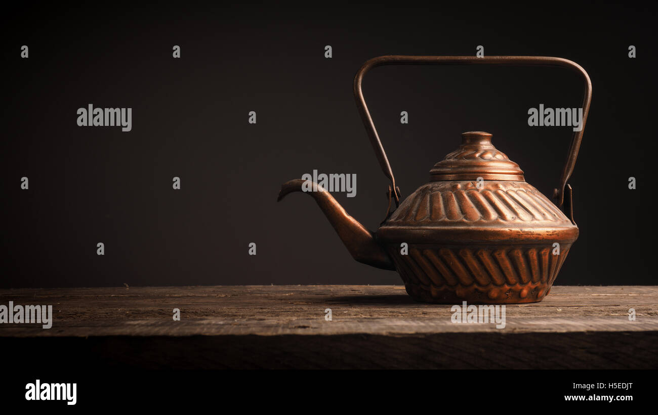 Old copper tea pot on a rustic wooden table with space for text Stock