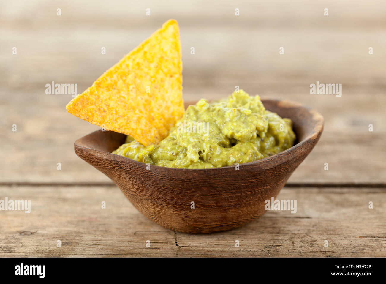 Tortilla chip in Guacamole sauce in wooden bowl on rustic table Stock Photo