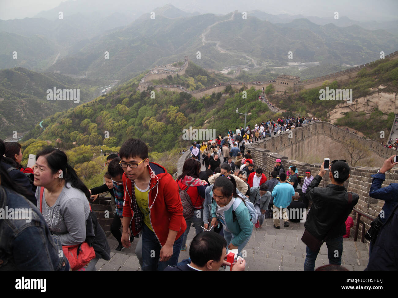 Thousands of tourists, some take photos with smartphones, climb the Great Wall of China going along the rugged mountains. Badaling near Beijing, China. Stock Photo