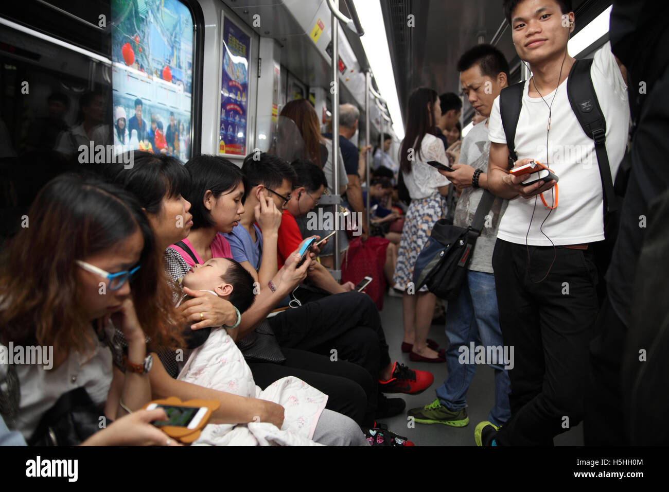 Chinese people ride the Guangzhou Metro train, lots of them play with smartphones and one mother is holding her sleeping baby. Stock Photo