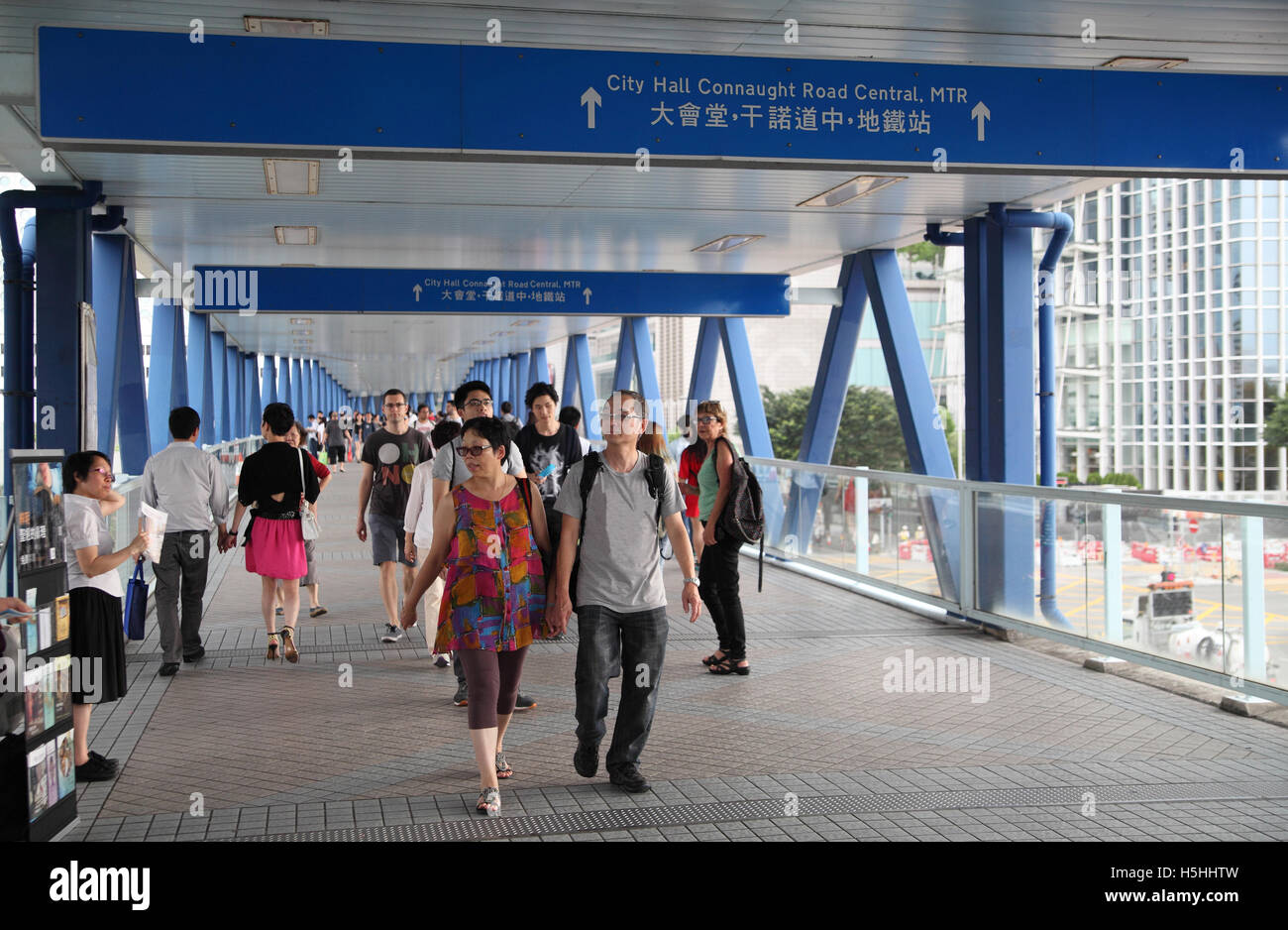 Chinese people are walking on a bridge going above a street,  bridges like this are very common in Hong Kong. Stock Photo