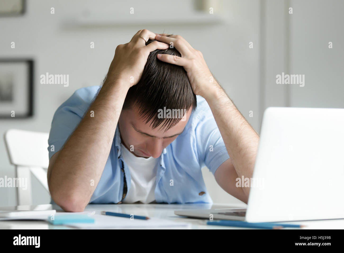 Portrait of man grabbing his head in despair near laptop Stock Photo