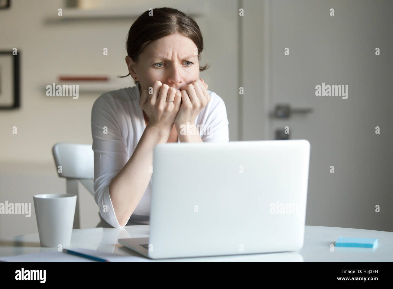 Portrait of a young woman at desk with laptop, fear Stock Photo