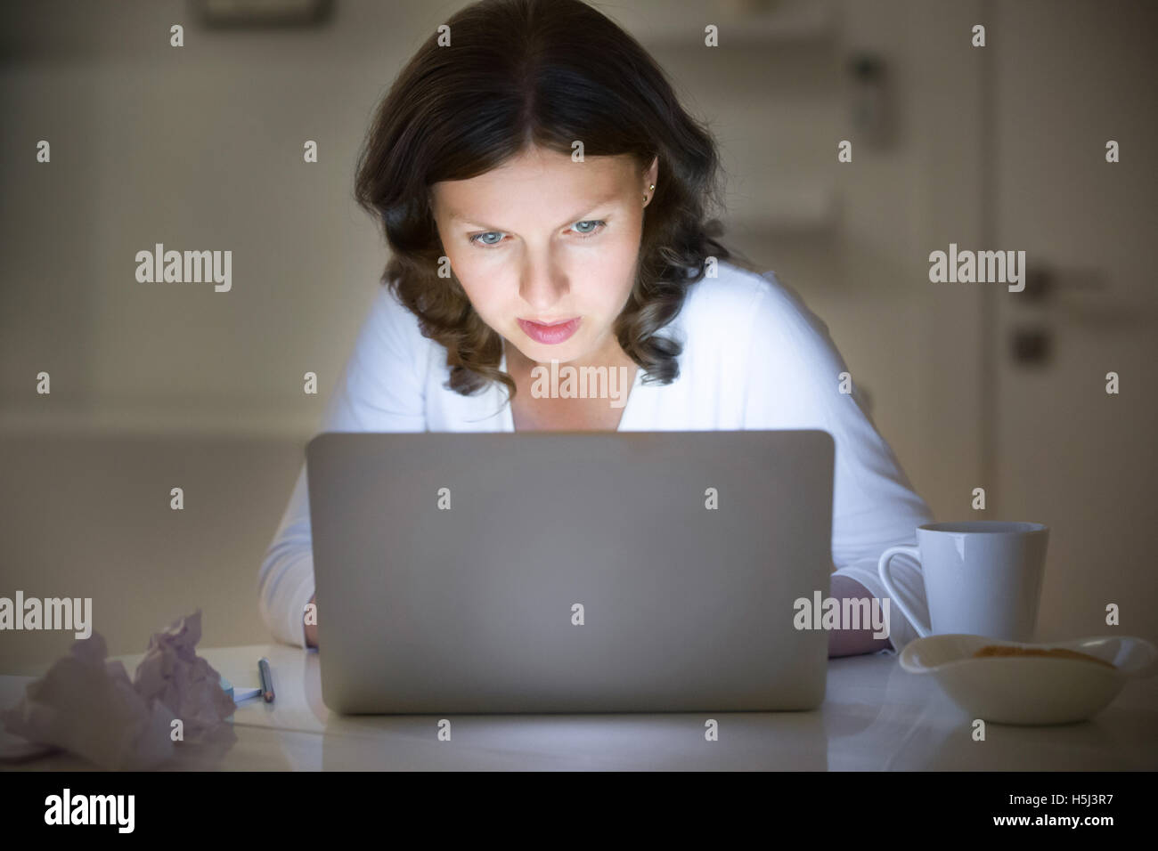Portrait of a woman at desk working with a laptop, late night Stock Photo