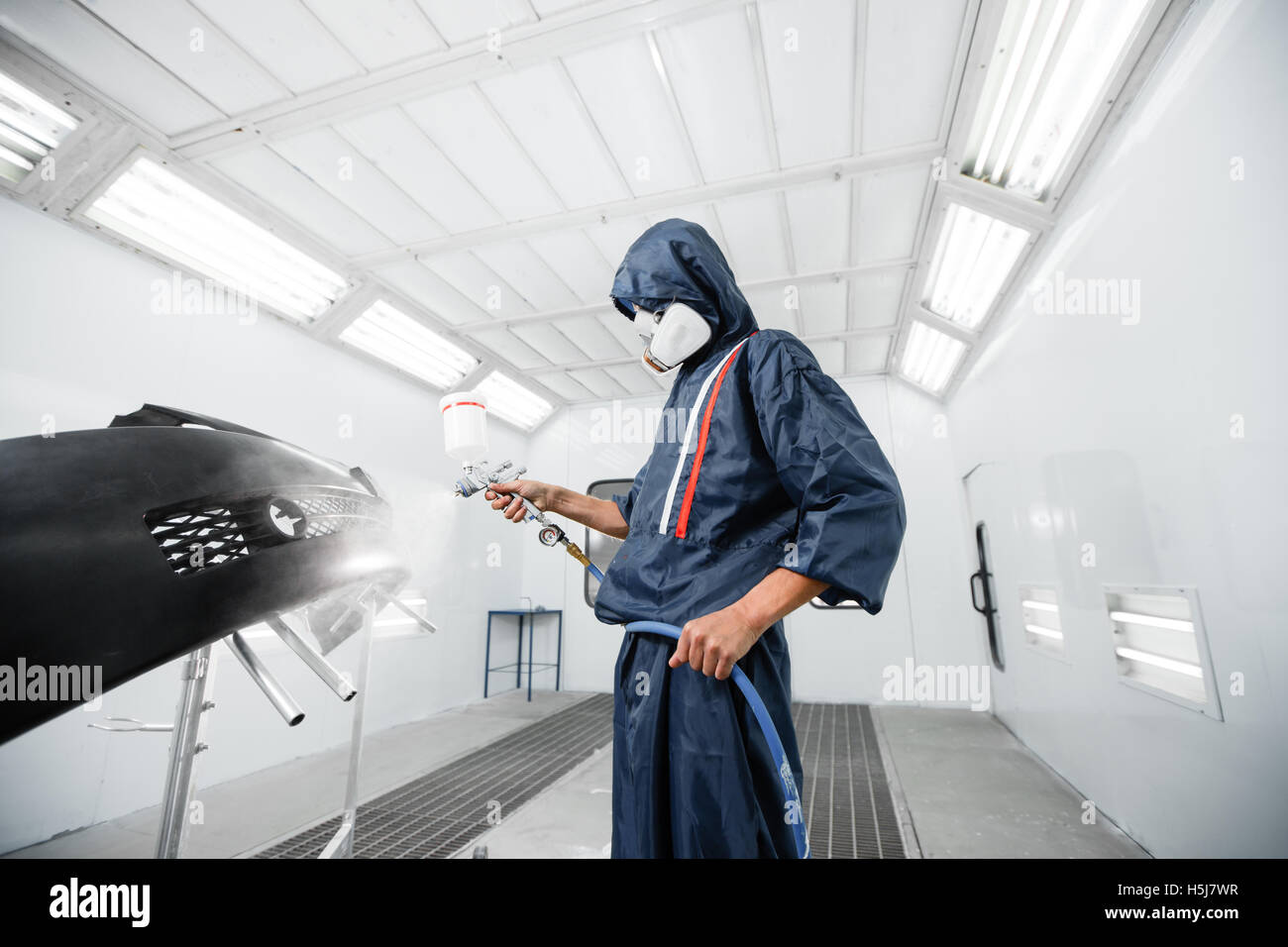 worker painting a car black blank parts in special garage, wearing