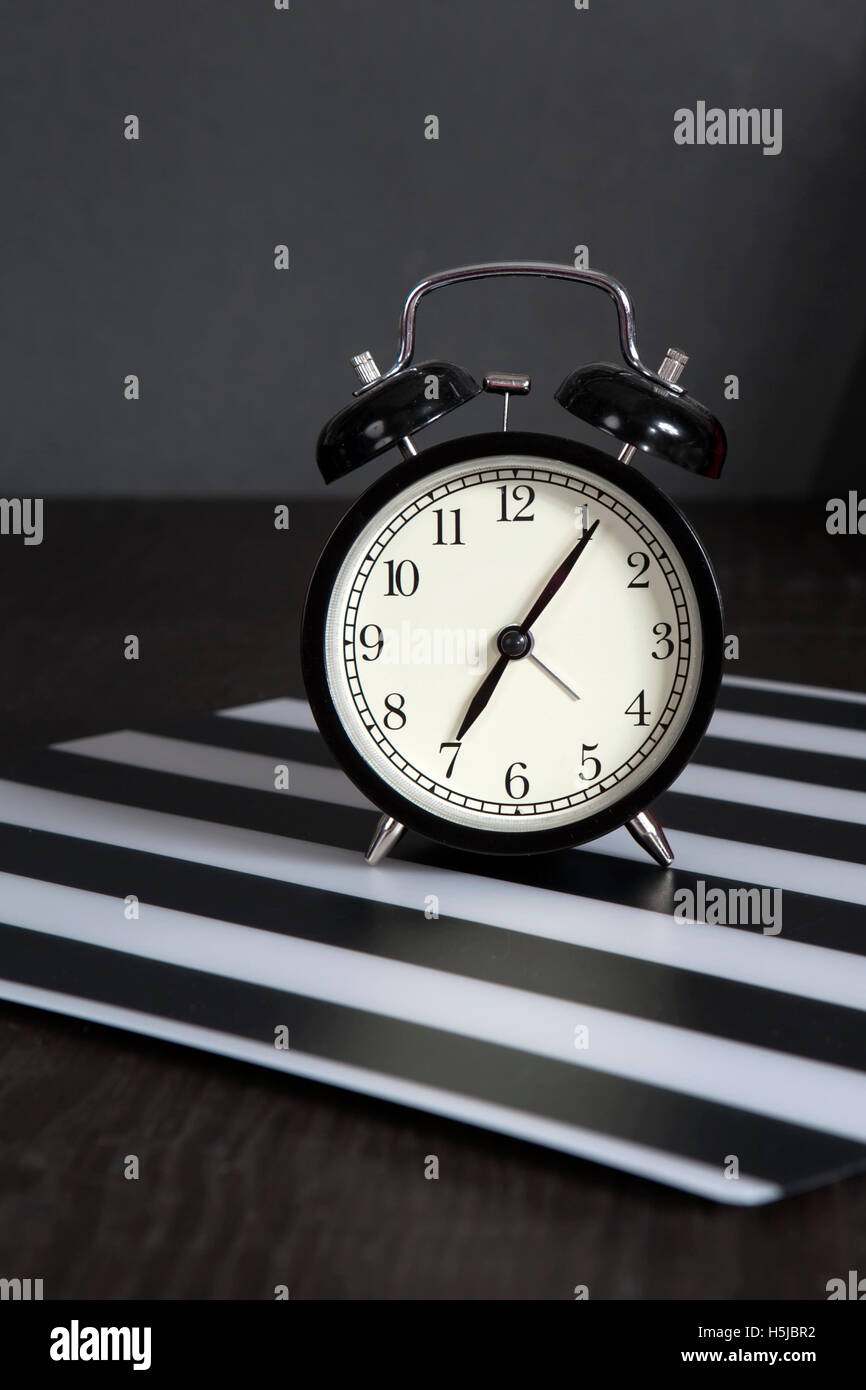the Black alarm clock on a black and white striped napkin showing 7 o'clock on a bedside table Stock Photo