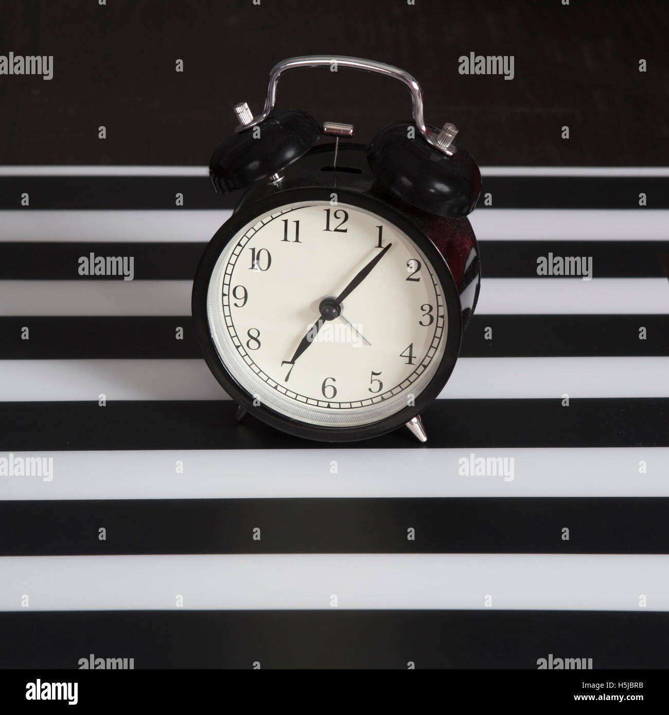 the Black alarm clock on a black and white striped napkin showing 7 o'clock on a bedside table Stock Photo