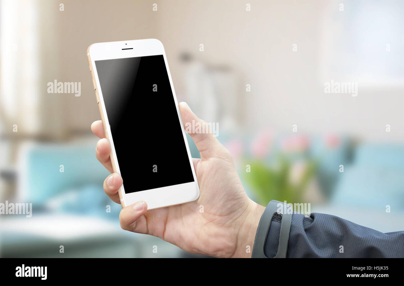 Using white silver smart phone in room. Blank screen of mobile device for mock-up. White background. Room interior in background Stock Photo
