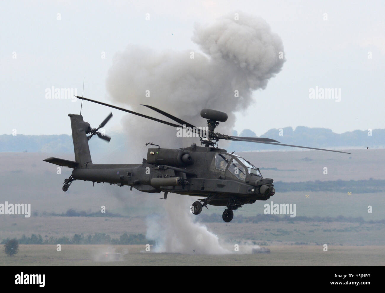 An Apache attack helicopter passes an explosion during an army combined arms manoeuvre demonstration at Larkhill Camp, Wiltshire. Stock Photo