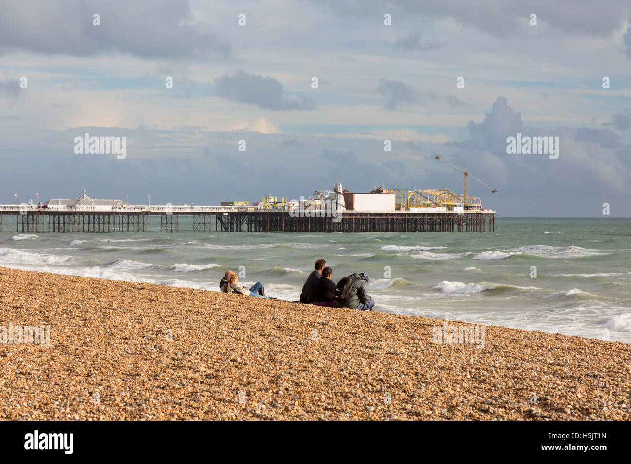 People sitting on Brighton beach looking at Brighton Pier in autumn, Brighton, East Sussex England UK Stock Photo