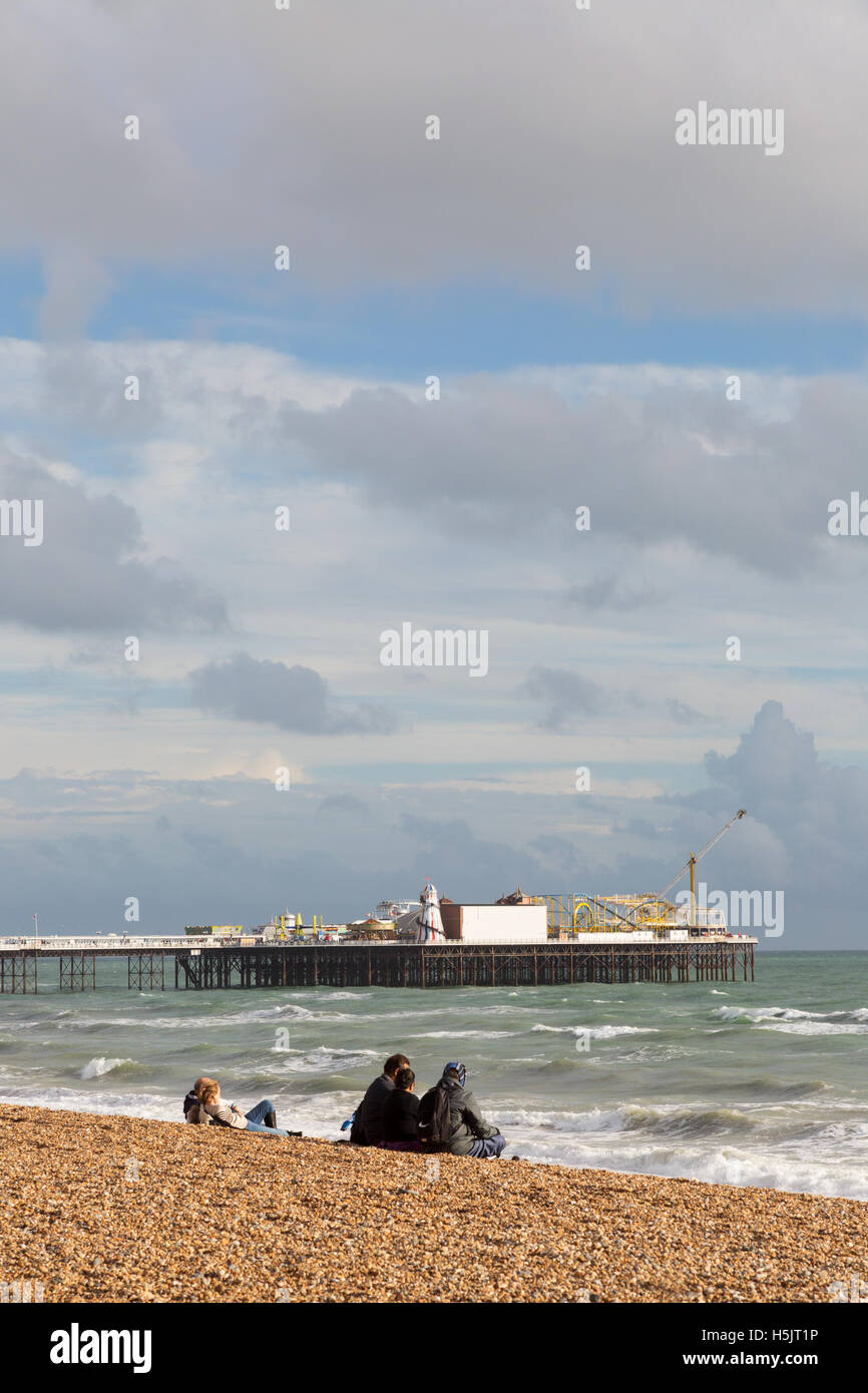 People sitting on Brighton beach looking at Brighton Pier in autumn, Brighton, East Sussex England UK Stock Photo