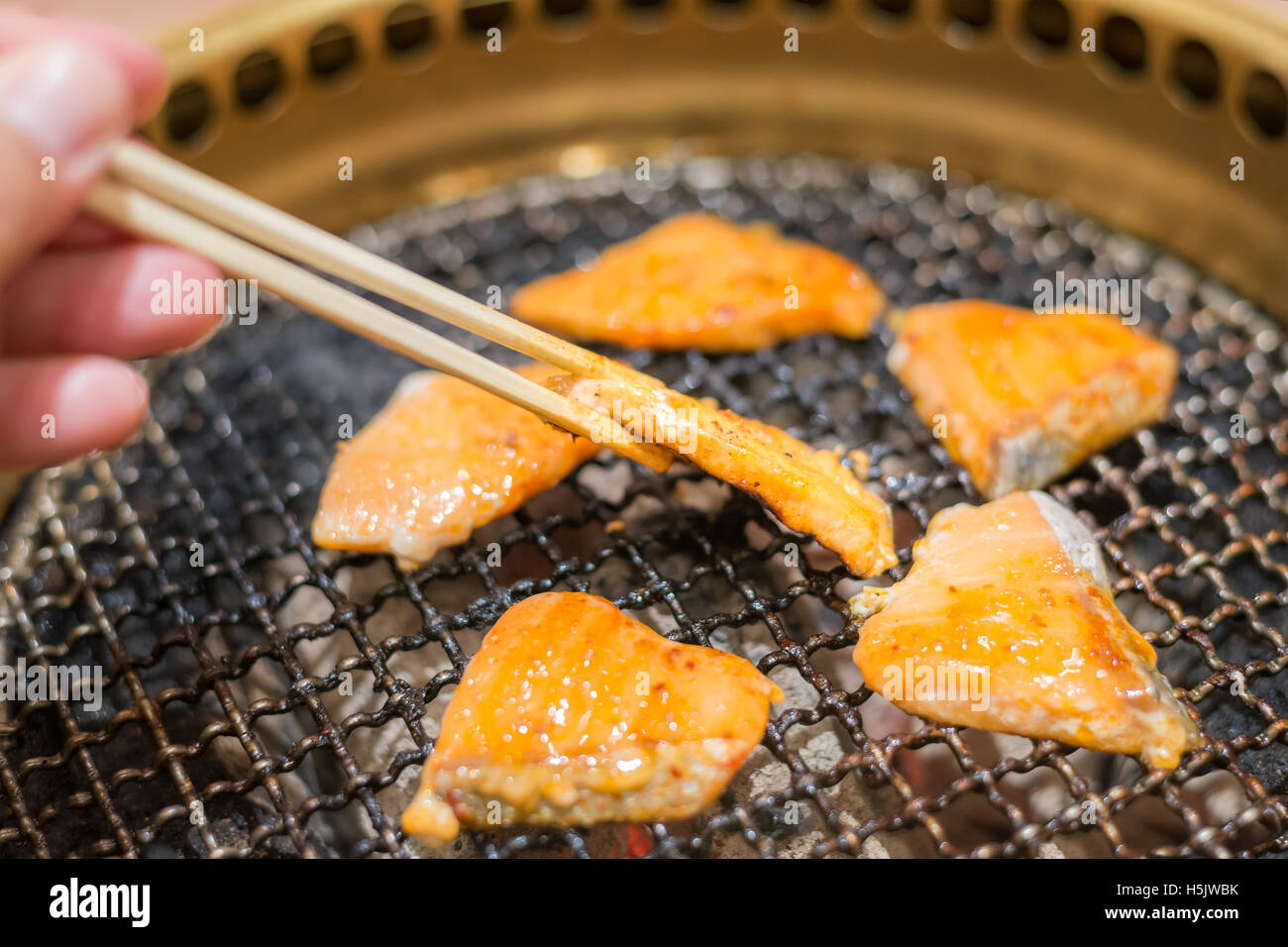 Salmon fish steak cooking over charcoal grill. Close up at chopstick