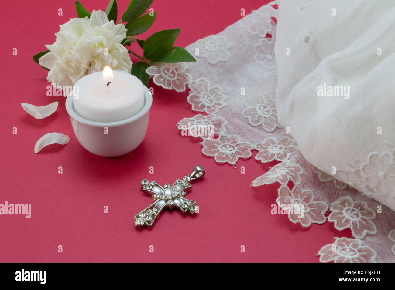 Red christening background with white vintage lace dress, candle and