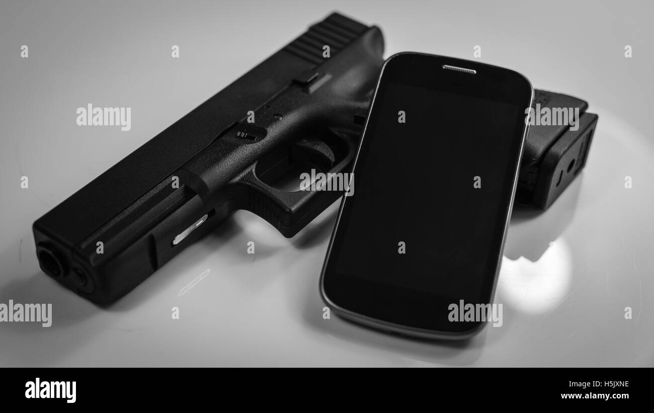 A gun and a modern smart phone, black and white Stock Photo