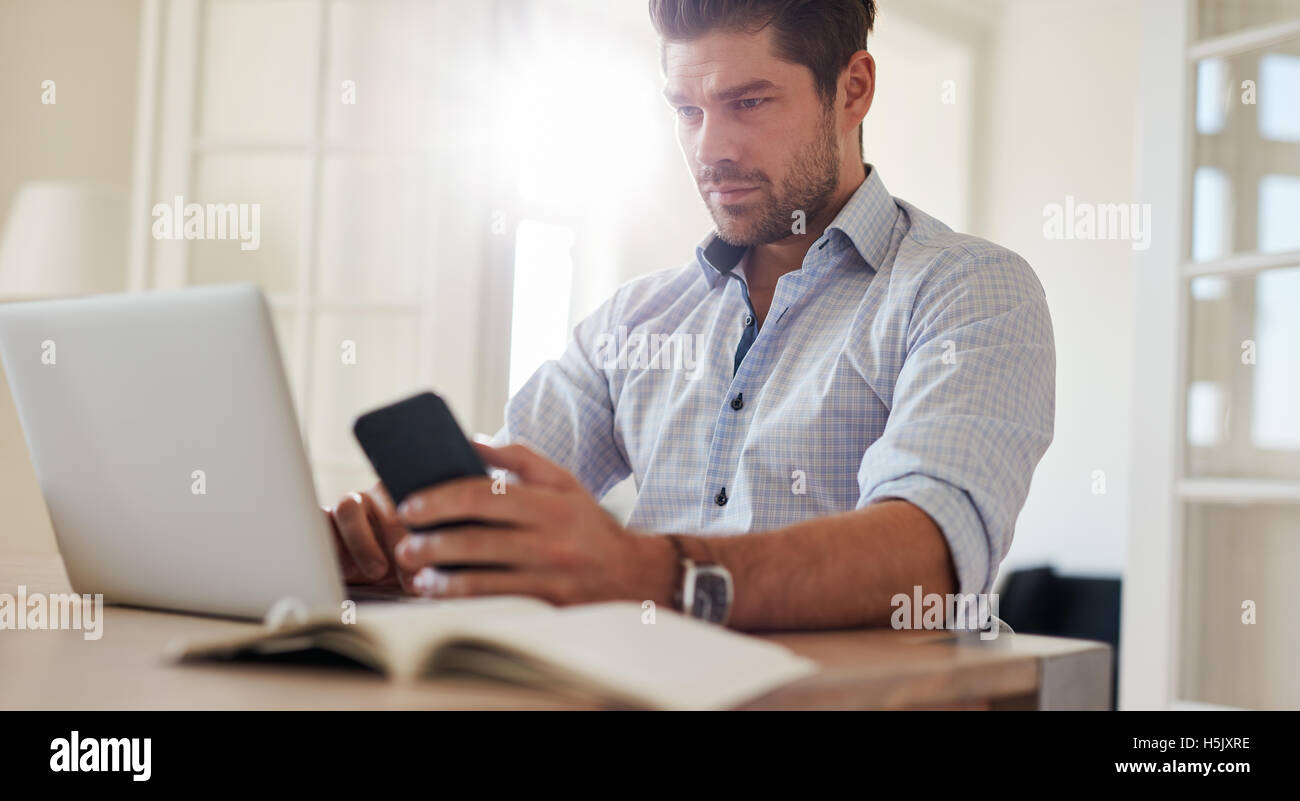 Shot of young man sitting at desk with mobile phone and laptop. Business man sitting at table using laptop computer and cellphon Stock Photo