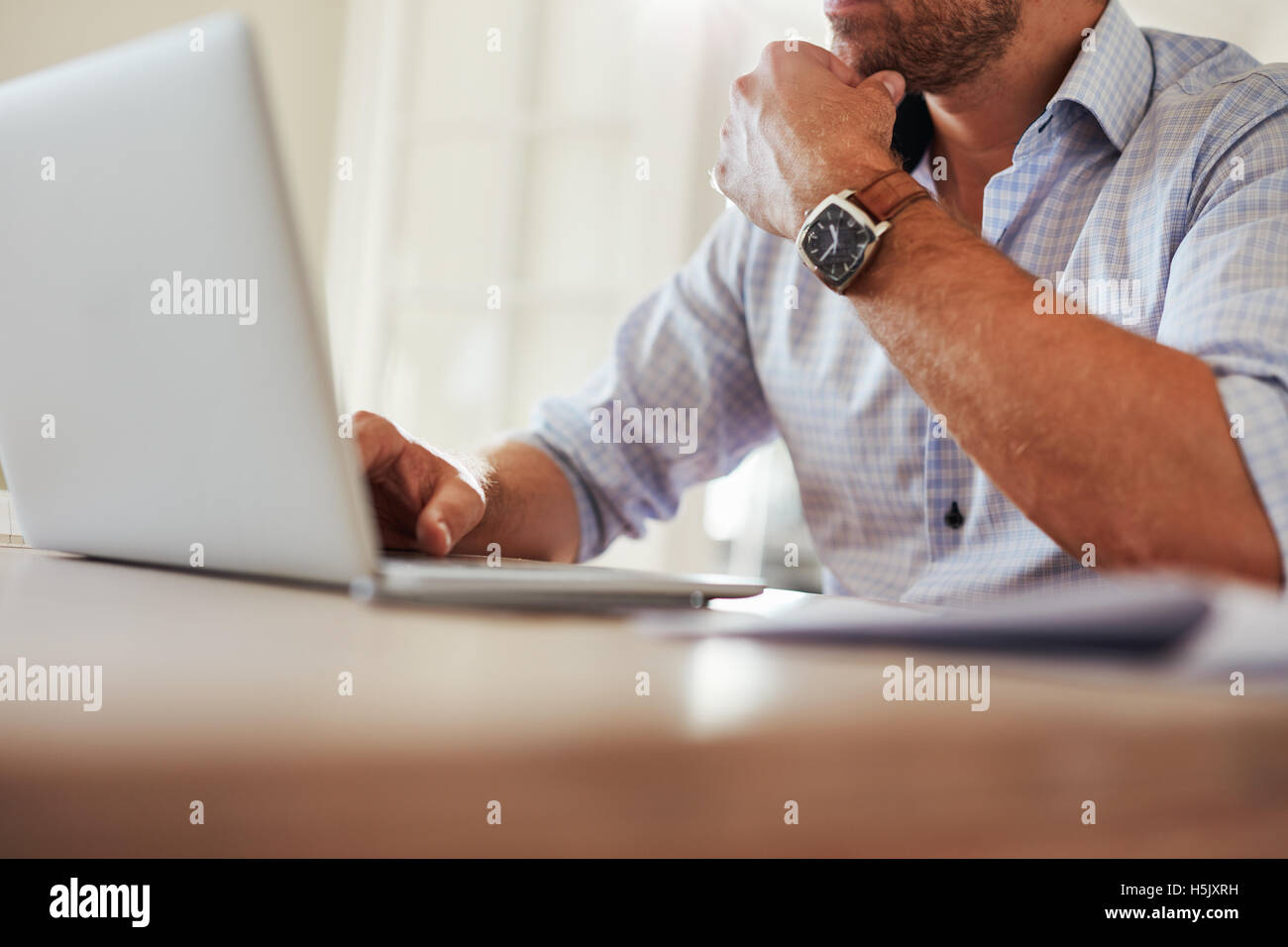 Close up shot of young man sitting at table and working on laptop. Businessman working from home. Stock Photo