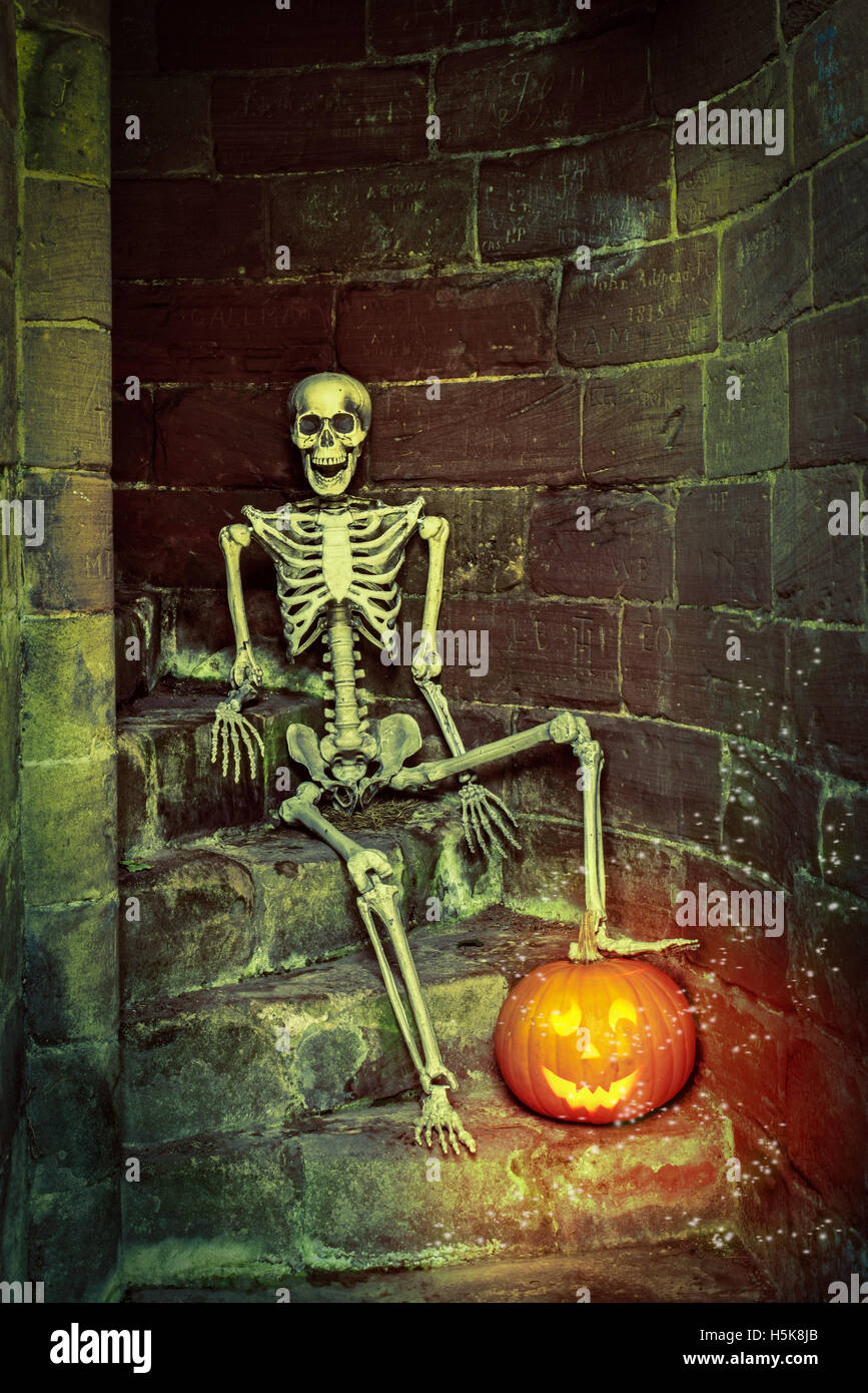 Skeleton with lit pumpkin on the steps in an ancient abbey Stock Photo