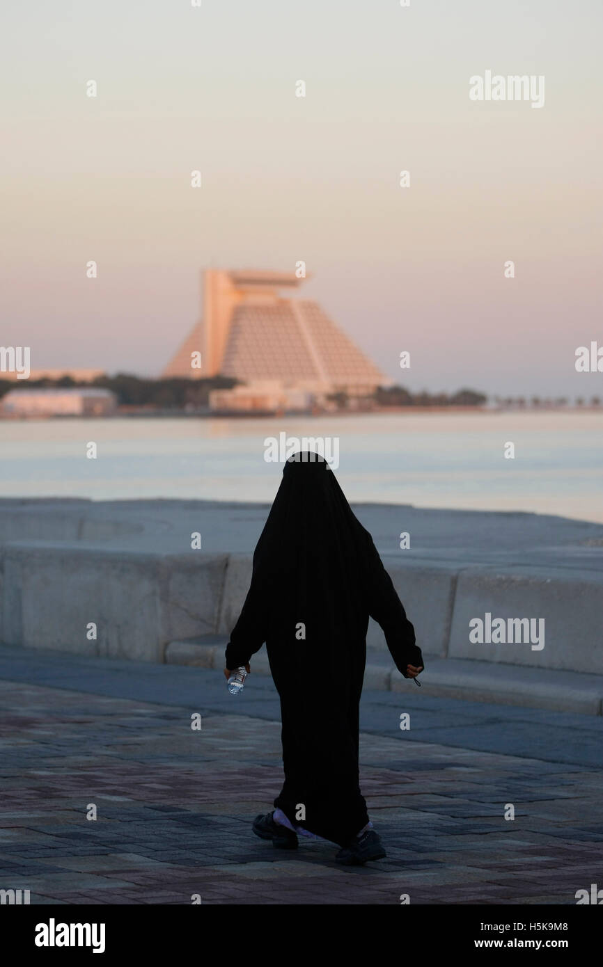 Arab woman wearing a traditional black robe, walking along the Corniche, Sheraton Hotel in the back, West Bay District, Doha Stock Photo