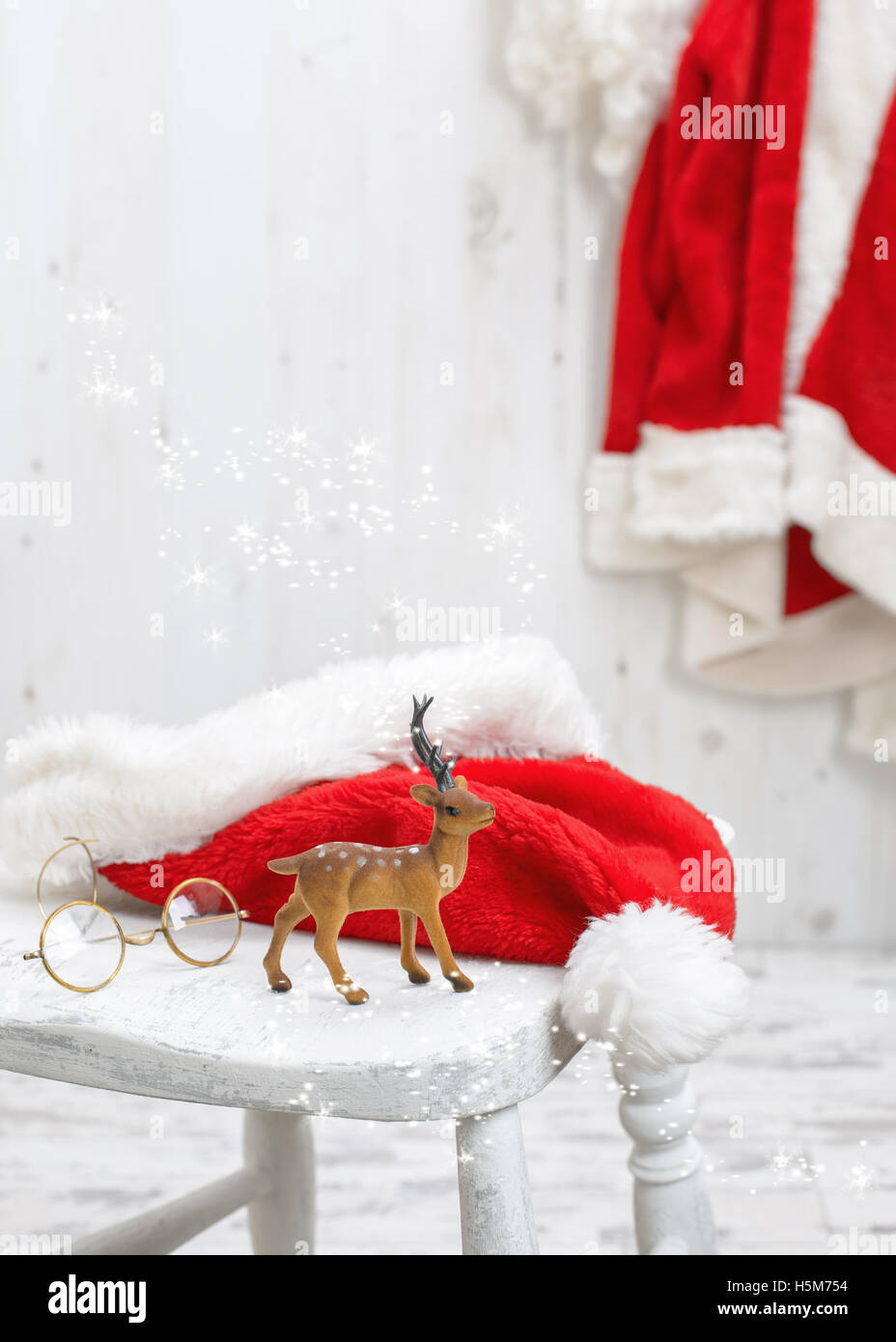 Reindeer with santa and spectacles hat on white stool Stock Photo