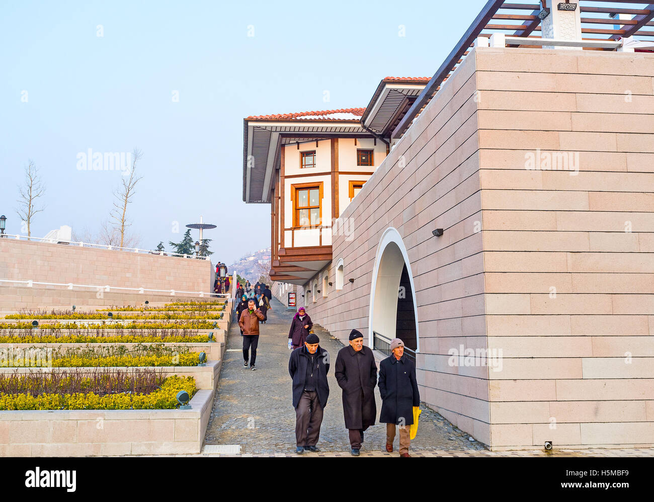The tourists and locals leave the Haci Bayram Mosque, walking along the modern street with green flower beds Stock Photo