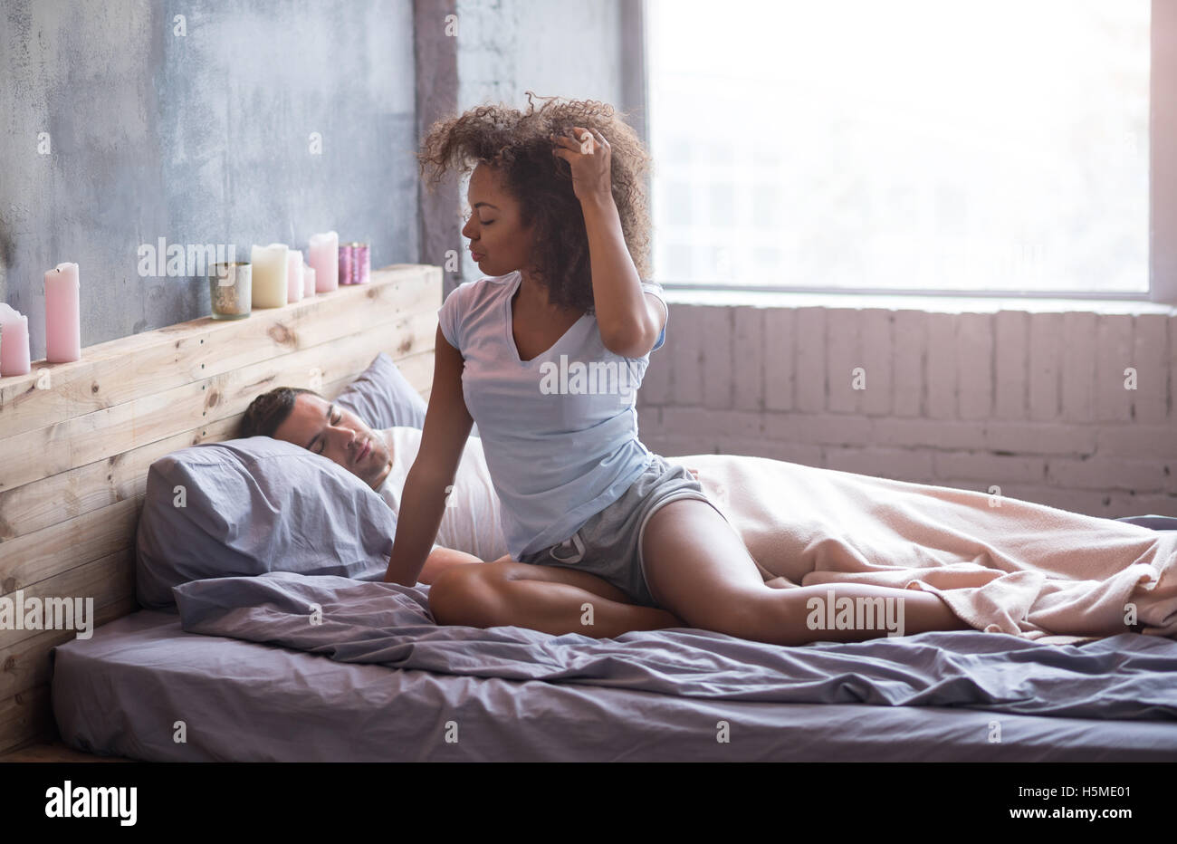Pretty girl sitting in bed while her husband is sleeping Stock Photo