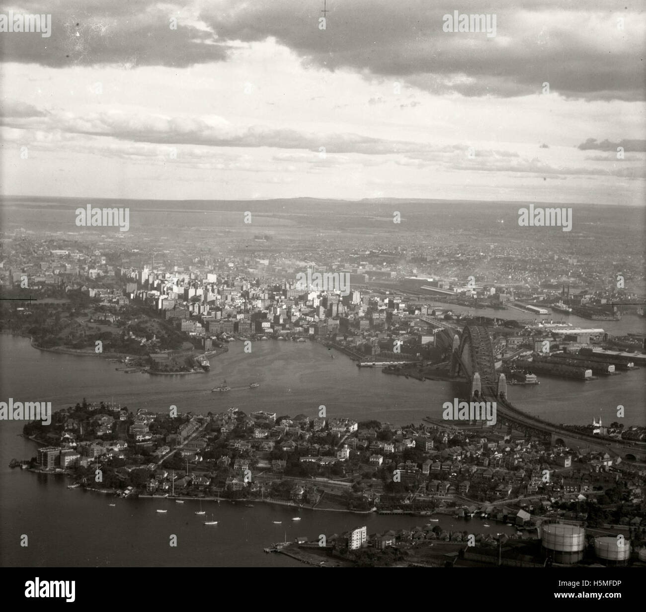 Aerial view of Kirribilli, Sydney, featuring the Harbour Bridge and the city skyline on 15 June 1937. This image was part of the Adastra Aerial Survey, documenting the urban landscape and architectural features of the area during the late 1930s. Stock Photo