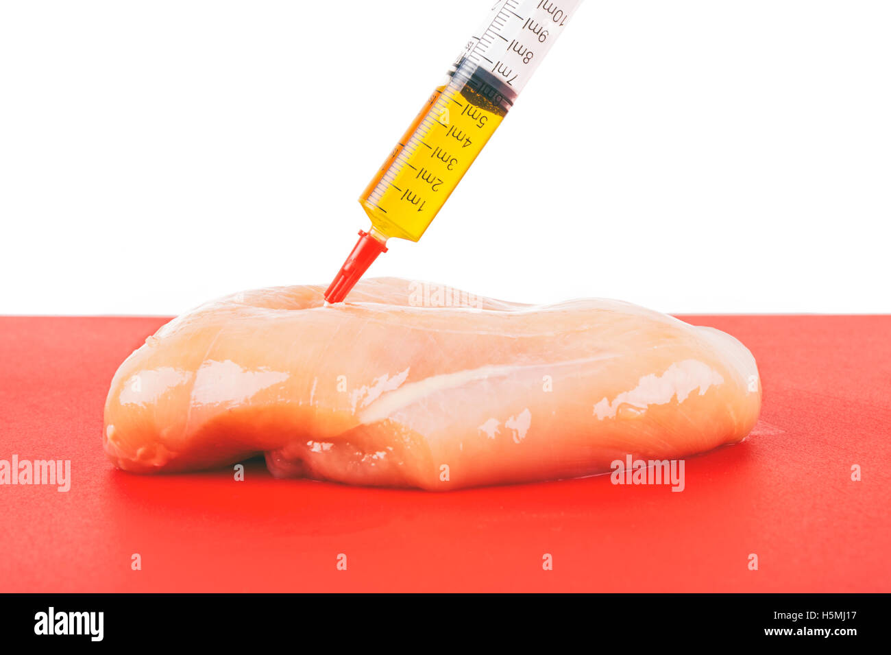 Syringe with liquid being injected to a piece of meat. Conceptual illustration for Hormones and antibiotics in food production. Stock Photo