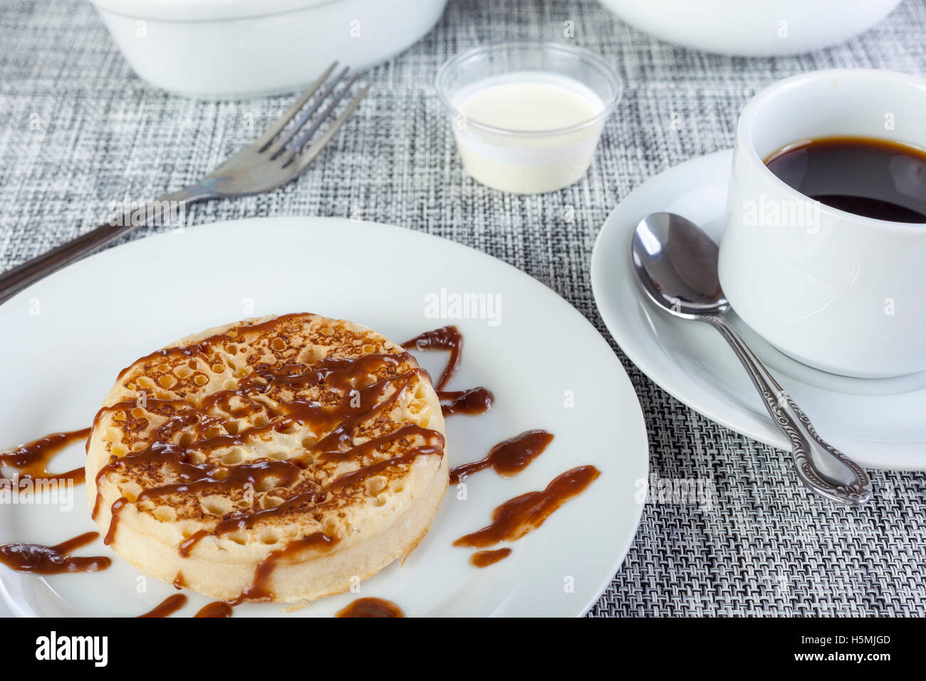 Sticky chocolate sauce on a freshly toasted crumpet with coffee on a breakfast table Stock Photo
