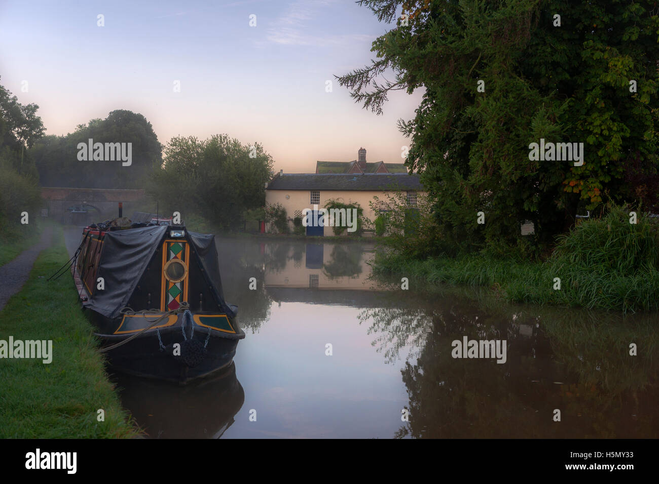 Moored narrowboat and a pretty cottage on the banks of the Moss Hall Winding Hole, Shropshire Union Canal, Audlem, Cheshire, UK Stock Photo