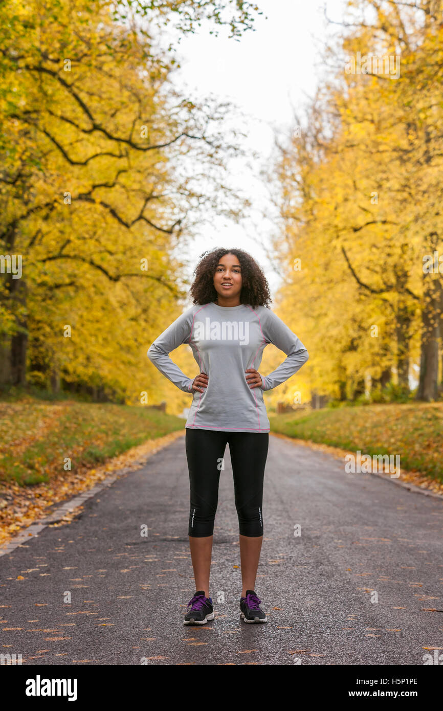 Beautiful mixed race African American young woman girl teenager fitness running jogging in Autumn Fall trees Stock Photo