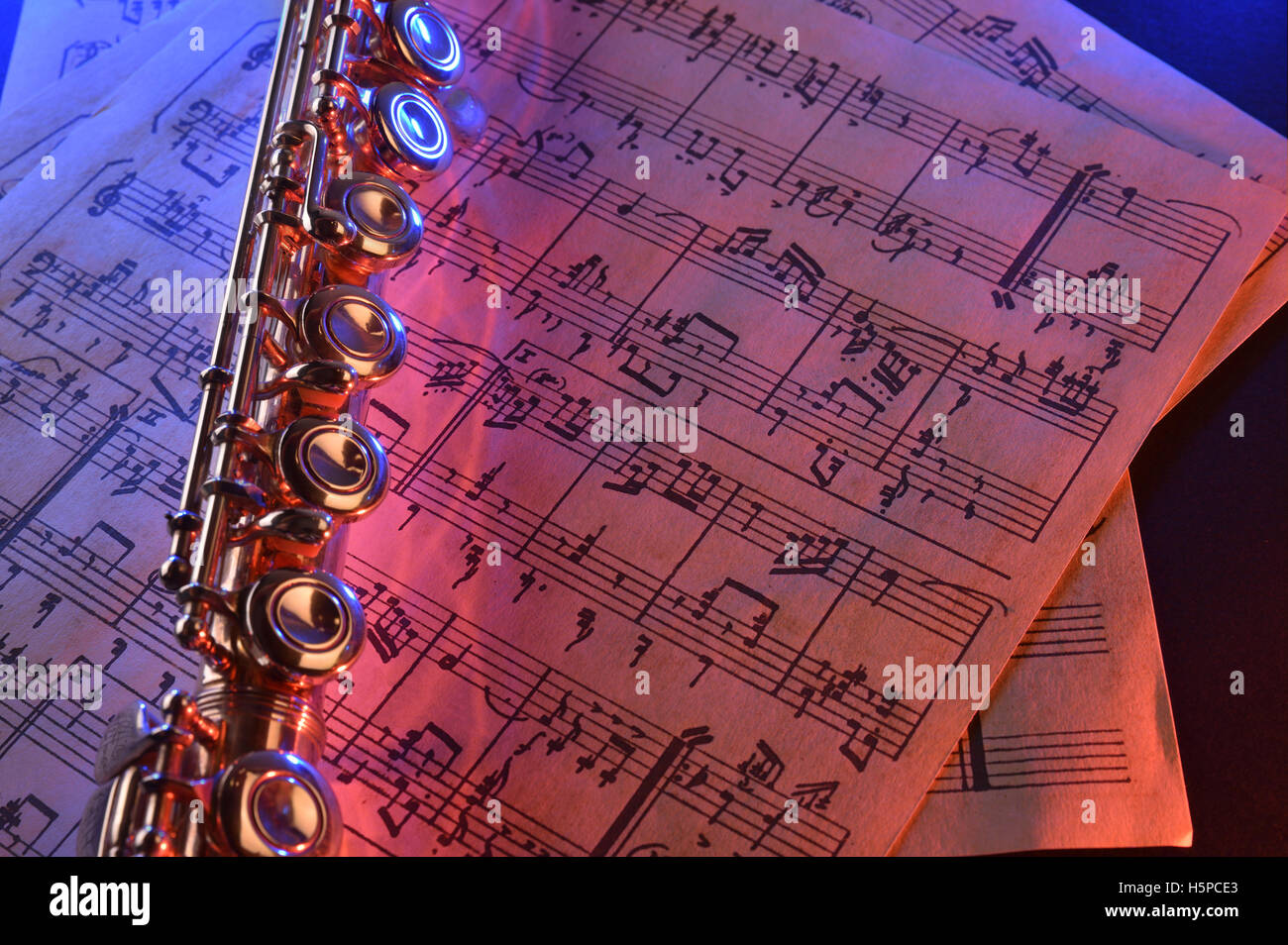 Transverse flute and old sheet music on black table red blue ...