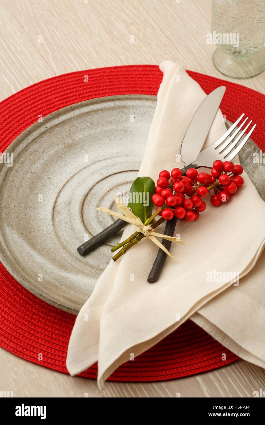 Festive casual Christmas table setting place setting with rustic silverware, handmade pottery plate and natural holly decoration Stock Photo
