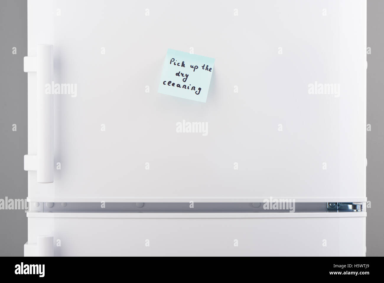Pick up the dry cleaning note on light blue sticky paper on white refrigerator door Stock Photo