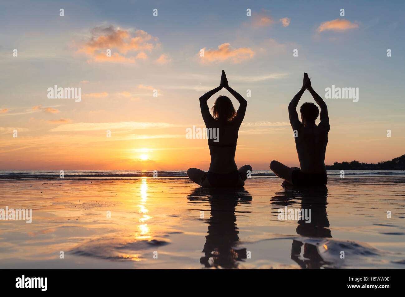 Two healthy young adults meditating with yoga for well-being on the beach at sunrise Stock Photo