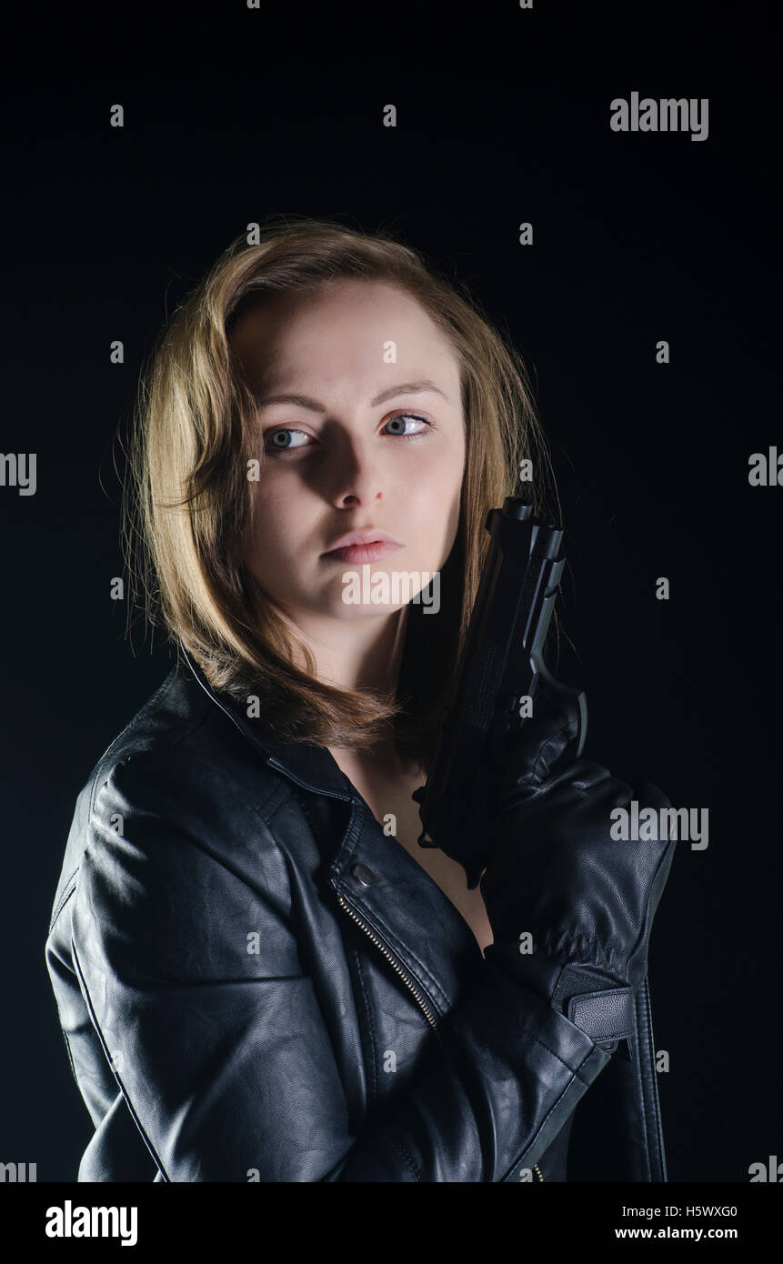 Blonde woman in black leather jacket holding a gun in the dark Stock Photo