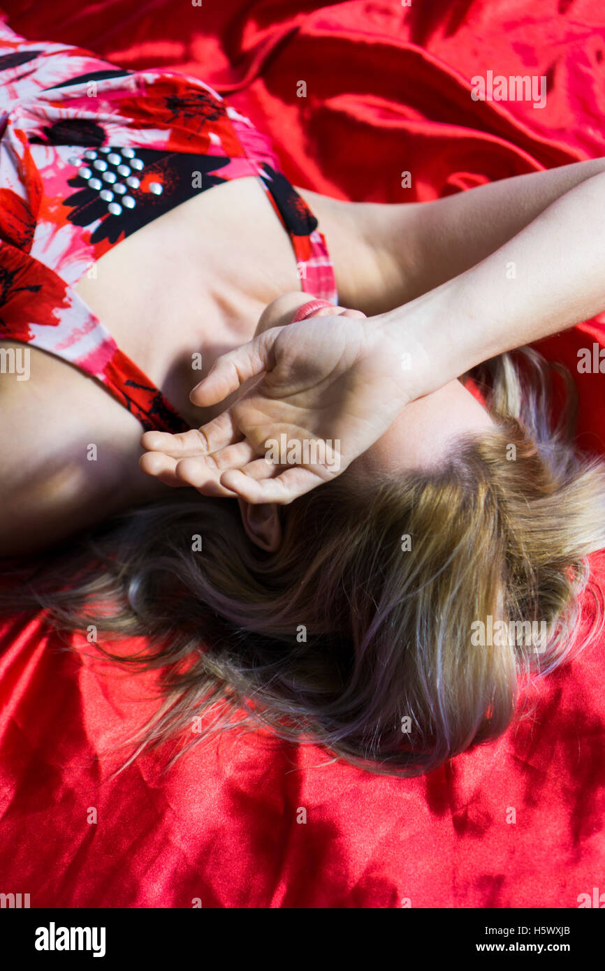 Depressed woman laying down in bed hiding face with hand Stock Photo
