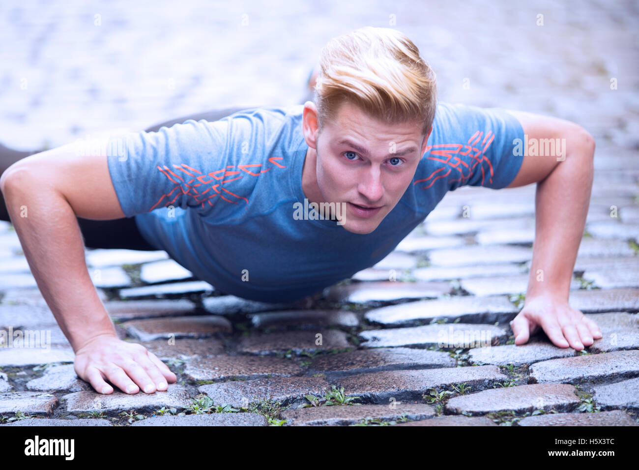young handsome man doing pushups outdoors on cobblestone Stock Photo